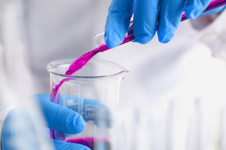 A male chemist holds test tube of glass in his hand overflows a liquid solution of potassium permanganate conducts an analysis reaction takes various versions of reagents using chemical manufacturingの写真素材