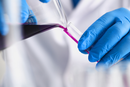 A male chemist holds test tube of glass in his hand overflows a liquid solution of potassium permanganate conducts an analysis reaction takes various versions of reagents using chemical manufacturingの写真素材