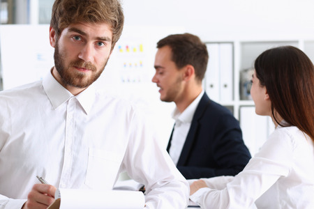Handsome smiling bearded man in office look in camera with colleagues in background. White collar worker, modern lifestyle, graduate college study, report idea, coach train visit, make note conceptの写真素材