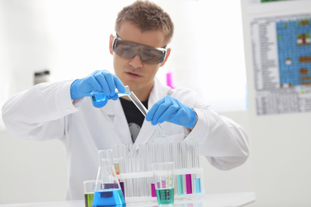 A male chemist holds test tube of glass in his hand overflows a liquid solution of potassium permanganate conducts an analysis reaction takes various versions of reagents using chemical manufacturingの写真素材