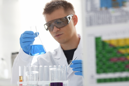 A male chemist holds test tube of glass in his hand overflows a liquid solution of potassium permanganate conducts an analysis reaction takes various versions of reagents using chemical manufacturingの写真素材