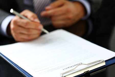 Male arm in suit and tie fill form clipped to pad with silver pen closeup. Sign gesture, read pact, sale agent, bank job, make note, loan credit mortgage investment, finance chief, legal law conceptの写真素材