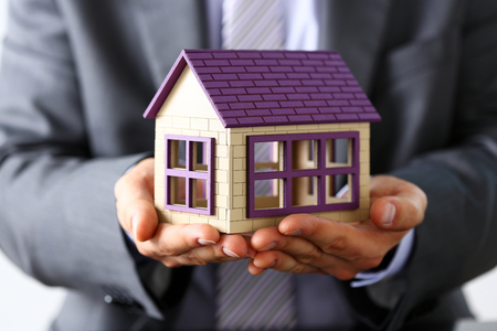 Man in suit and tie cover with arms little toy house closeup. Palm shelter, save and trust, defende owner wealth, sell or rental structure, loan idea, no problems, buy defence, future plan conceptの写真素材