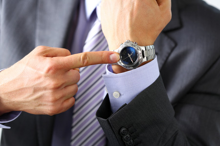 Man in suit and tie check out time at silver wristwatch closeup. Show and point with finger, waste minute, modern punctual life style, start hurry, job idea, last second, clockwork precision conceptの写真素材