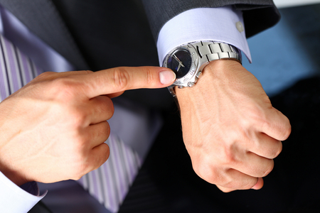 Man in suit and tie check out time at silver wristwatch closeup. Show and point with finger, waste minute, modern punctual life style, start hurry, job idea, last second, clockwork precision conceptの写真素材