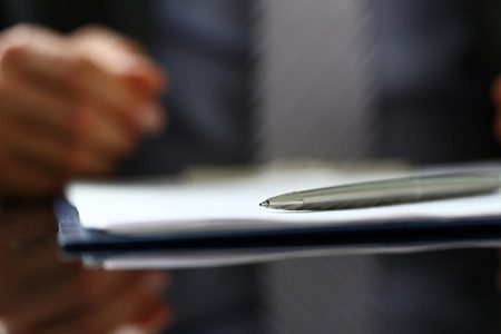 Silver pen lying on form clipped to pad closeup with male in suit and tie in background. Sign gesture, read pact, sale agent, bank job, make note, loan credit mortgage investment, finance chiefの写真素材