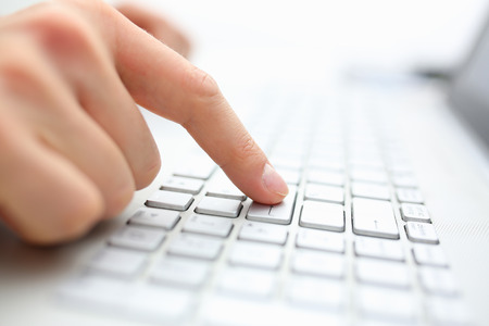The male hand finger presses the enter key on the laptop keyboard. Confirms the completed purchase...