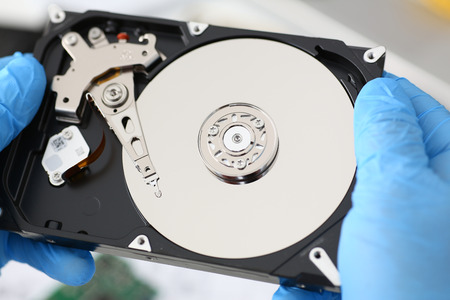 A male repairman wearing blue gloves is holding a hard drive from a computer or laptop in his hands....