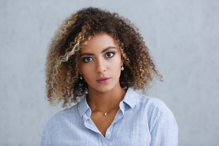 Beautiful black woman portrait. It's a gray background and does not smile beauty fashion style mulatto curly hair with white strands look the eye into the cameraの写真素材