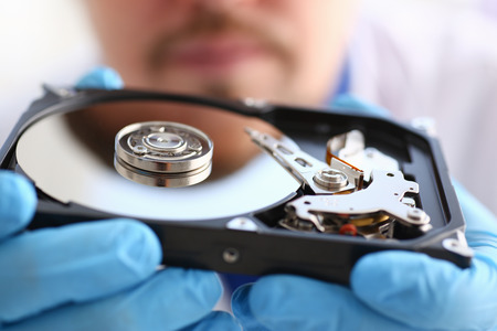 A male repairman wearing blue gloves is holding a hard drive from computer or laptop in hands....