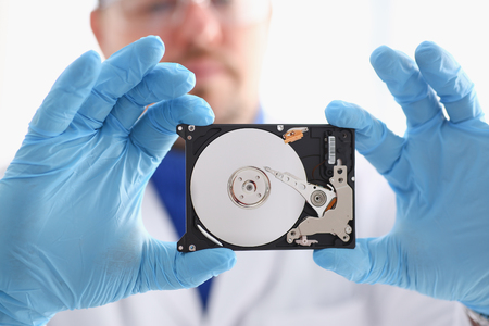 A male repairman wearing blue gloves is holding a hard drive from computer or laptop in hands....