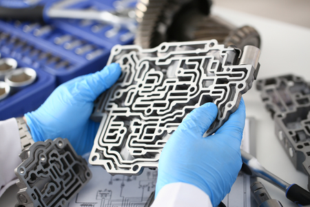 The auto repair service repairman in automatic gearboxes holds in his hand in blue protective gloves the hydroblock detail dehydrates the diagnostics and estimates the detail test transmission closeupの写真素材