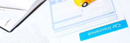 Insurance form lying on table with unrecognizable yellow toy car closeup. Driver money loss...