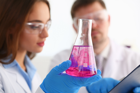 Female and male chemist holds test tube of glass in his hand overflows liquid solution of potassium permanganate conducts an analysis of water samples versions of reagents using chemical manufacturingの写真素材