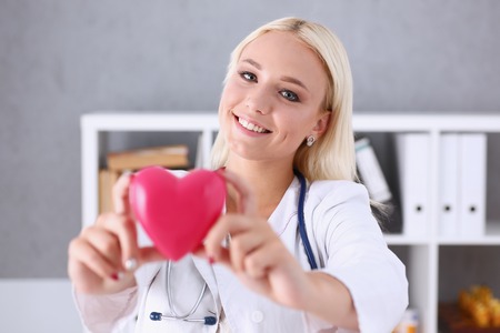 Beautiful smiling doctor hold in arms red heartの写真素材