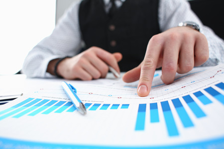 Male arm hold silver pen and point finger in financial graphの写真素材