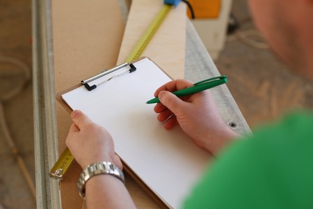 Arms of worker making notes on clipboard with green pen