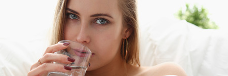 blond woman hold glass of water in arm early morning stay in bedの写真素材