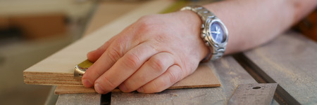 Arms of worker measuring wooden bar closeup