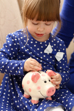 Child little girl arm putting coins into piggybankの写真素材
