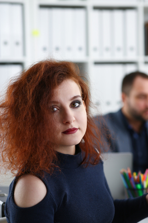 young beautiful red haired woman sit at table in office in cabinet of her bossの写真素材