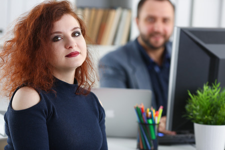 young beautiful red haired woman sit at table in office in cabinet of her bossの写真素材