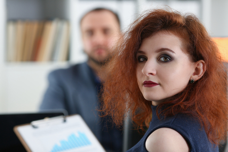 young beautiful woman sit on chair at table in office in cabinet of her boss hold binder in armsの写真素材