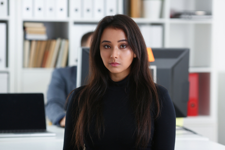 young beautiful brunette woman sit at table in office in cabinet of her bossの写真素材