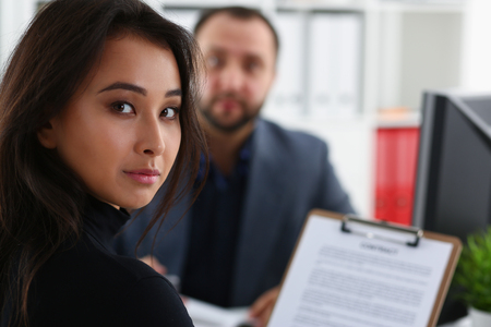 young beautiful woman sit on chair at table in office in cabinet of her boss hold binder in armsの写真素材