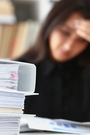 Tired and exhausted woman looks at documents propping up her head with her hands