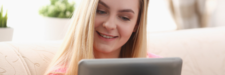 young beautiful blond woman sit on the sofa in livingroom hold tablet in armsの写真素材