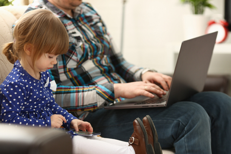Cute little girl on couch with dad use cellphoneの写真素材