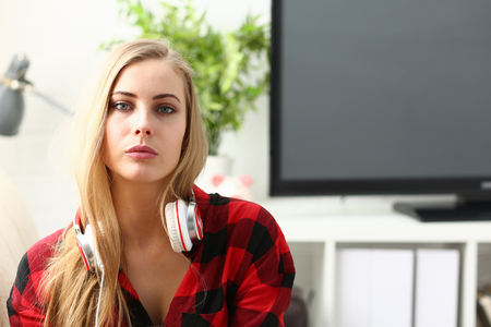 pretty blond young woman sit on sofa earphonesの写真素材