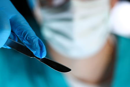 Surgeon arms in sterile uniform holding sharp knifeの写真素材