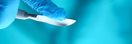 Surgeon arms in sterile uniform holding sharp knifeの写真素材