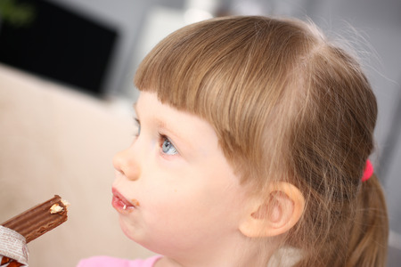 Little girl eating sweet chocolate candy with trace at her mouthの写真素材