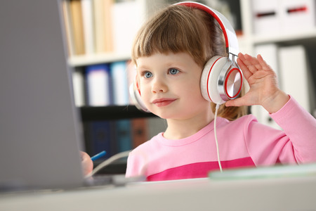 Little girl wearing headphones use mobile computerの写真素材