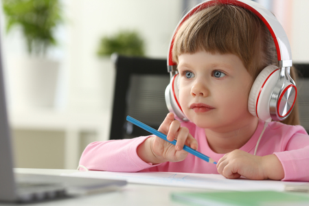 Little girl wearing headphones use mobile computerの写真素材