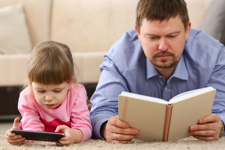 Father and daughter lie on floor using mobile phoneの写真素材