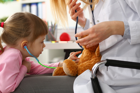 Little girl hold in arms toy stethoscope playing with teddy bearの写真素材