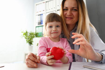 Little baby girl visiting doctor holding in hands red toy heartの写真素材