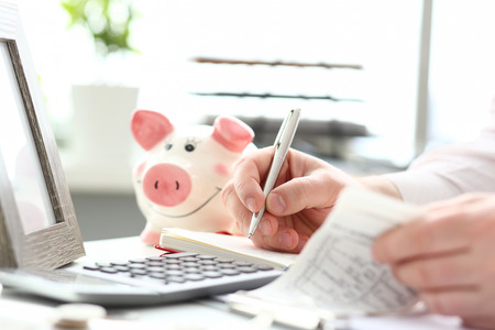 Male hands making notes with silver pen about family budgetの写真素材