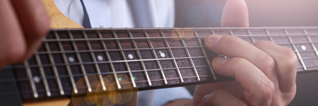 Male arms holding and playing classic shape wooden electric guitar closeup. Six stringed learning...