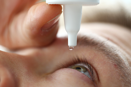 Male hand putting liquid drops in his eye solving vision problemの写真素材