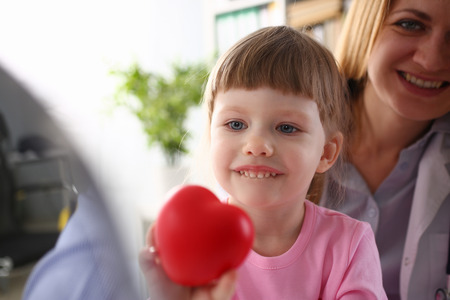 Little baby girl visiting doctor holding in hands red toy heartの写真素材