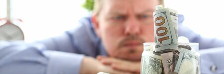 Man looking at jar full of money thinking about his debts