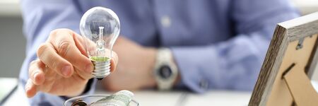 Male arm holding lightbulb over tip can full of US moneyの写真素材