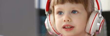 Little girl wearing headphones use mobile computerの写真素材