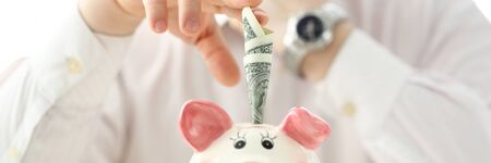 Male hand putting paper money into funny piggybank slotの写真素材