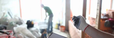 Skilled craftsman checking everything in unfinished room wondering if can be enough for start of process. Focus on man hands writing something down in special tablet. Building conceptの写真素材